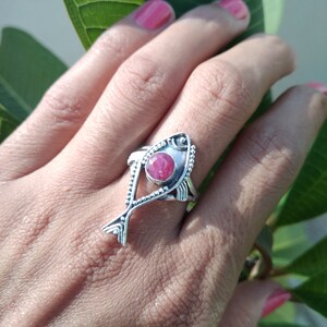 May include: A silver ring with a pink gemstone set in a fish design.