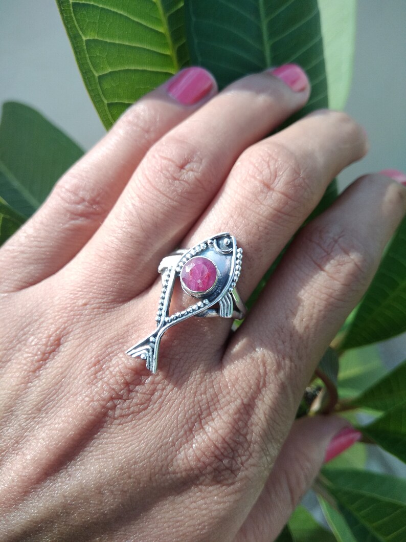 May include: A silver ring with a pink gemstone set in a fish design.