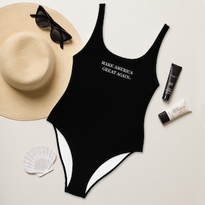 May include: Black one-piece swimsuit with white trim and the text "Make America Great Again." printed on the front.