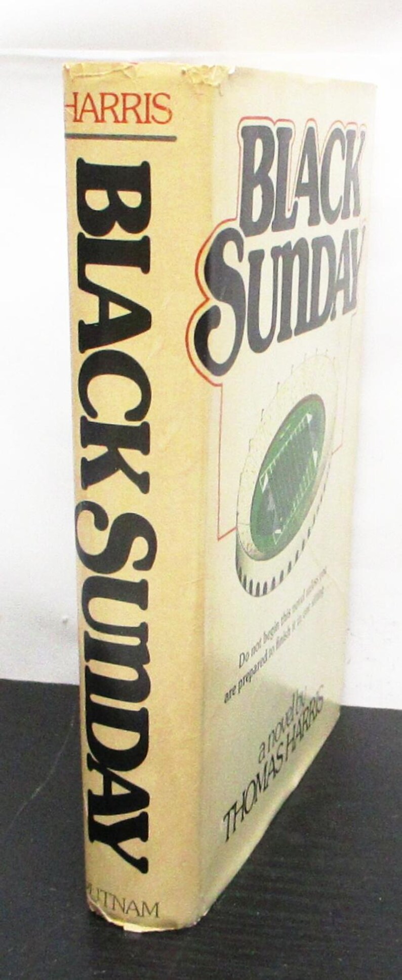 May include: A book titled "Black Sunday" by Thomas Harris. The cover is beige with black lettering and a stadium graphic. The author's name is printed at the bottom. The book is published by Putnam.