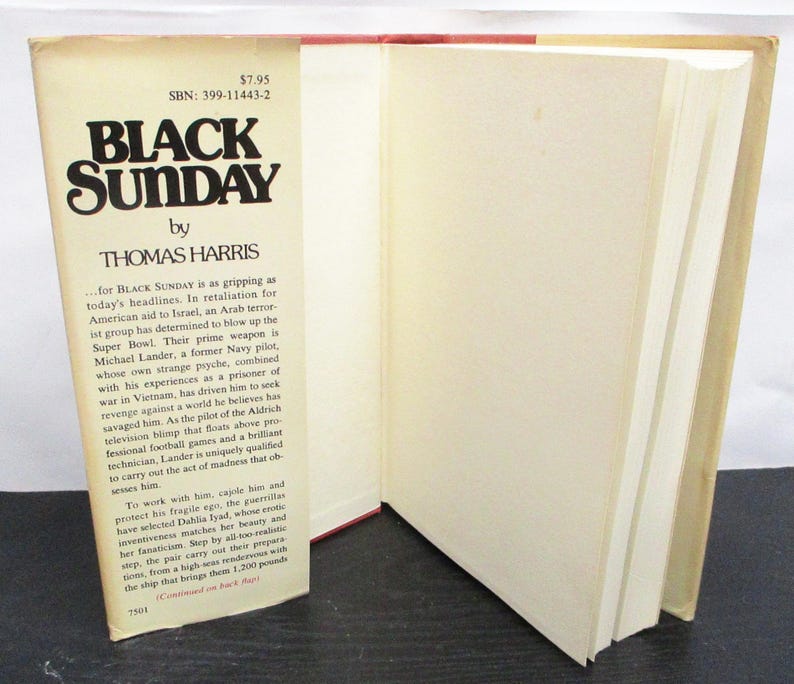 May include: A vintage hardcover book, "Black Sunday" by Thomas Harris, with a cream-coloured cover and black lettering. The book is open, displaying the text and pages. The spine is red.