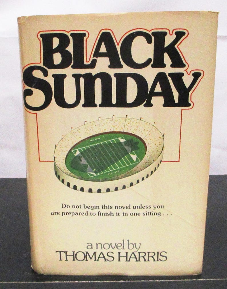 May include: A vintage paperback book titled "BLACK SUNDAY" by Thomas Harris. The cover shows a stadium illustration with a green field. The text reads, "Do not begin this novel unless you are prepared to finish it in one sitting..."