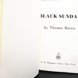 May include: An open book displaying the title "BLACK SUNDAY" by Thomas Harris. The book has a white cover with black lettering. The publisher's logo and name, G. P. Putnam's Sons, New York, are also visible.