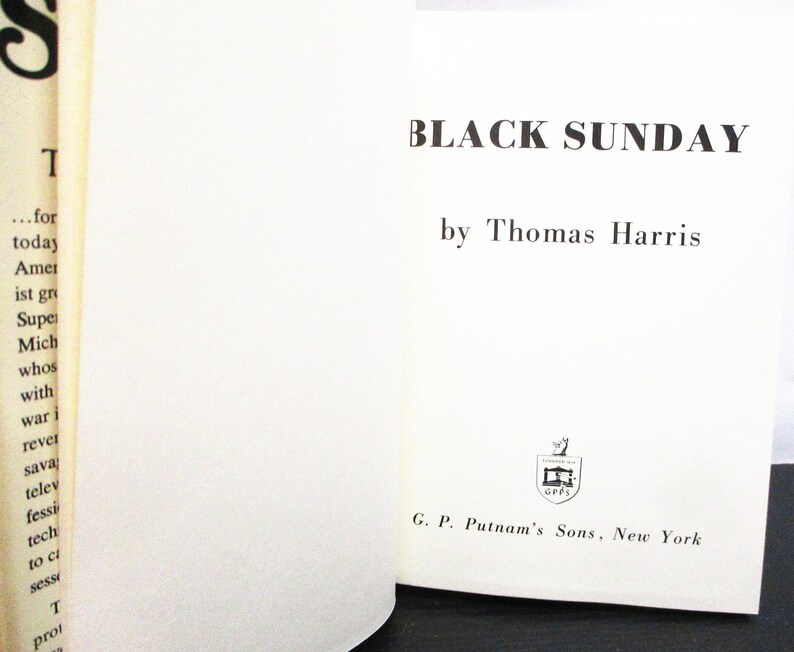May include: An open book displaying the title "BLACK SUNDAY" by Thomas Harris. The book has a white cover with black lettering. The publisher's logo and name, G. P. Putnam's Sons, New York, are also visible.