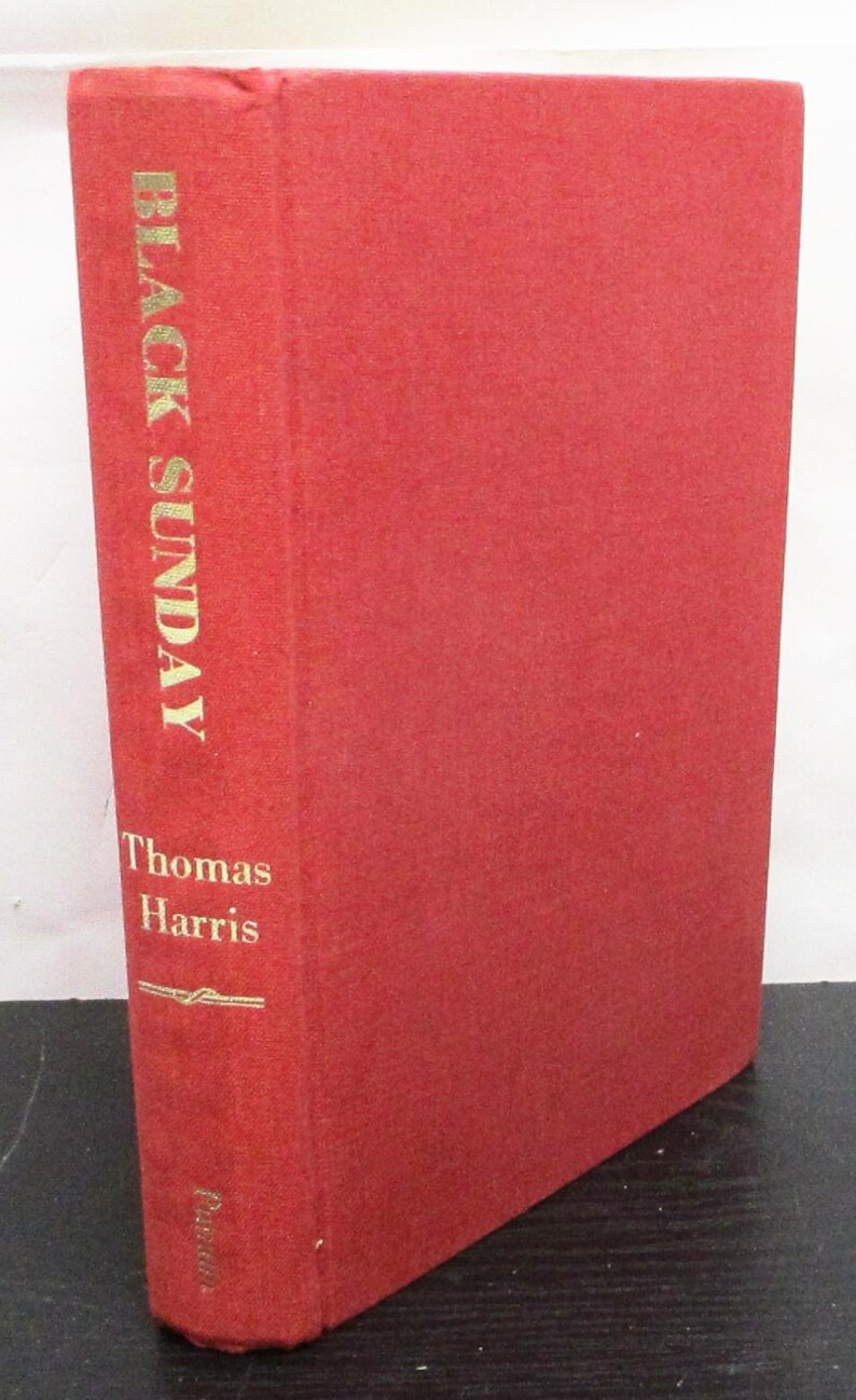May include: A red hardcover book titled "Black Sunday" by Thomas Harris. The book's spine features the title and author's name in gold lettering. The cover is a solid red colour.