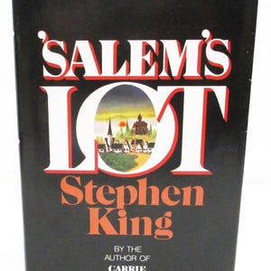 Peut inclure: Un livre relié intitulé Salem's Lot de Stephen King avec une jaquette noire. La couverture présente de grandes lettres blanches avec des contours rouges et une petite illustration colorée d'une ville avec une église et une grande maison.