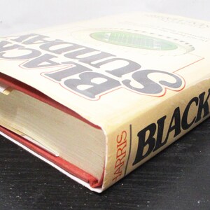 May include: A hardback book titled "Black Sunday" by Thomas Harris. The book has a beige cover with black and grey lettering. The edges of the pages are gold, and the spine is red.