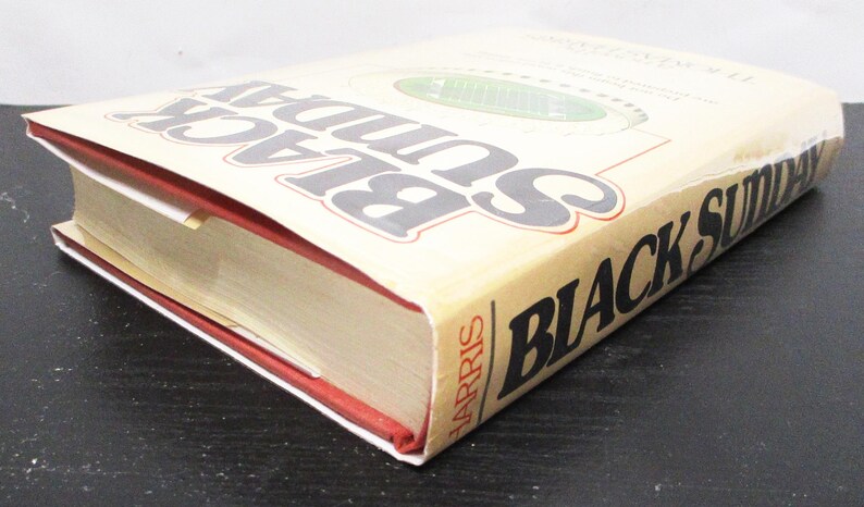 May include: A hardback book titled "Black Sunday" by Thomas Harris. The book has a beige cover with black and grey lettering. The edges of the pages are gold, and the spine is red.