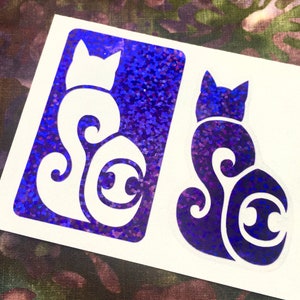 May include: Two purple glitter cat stickers with a stylized design. The cat is curled up with its tail wrapped around its body. The design includes a circle with a crescent moon inside.