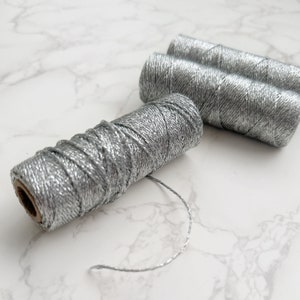 May include: Three spools of silver metallic thread. The thread is wound around cardboard spools.
