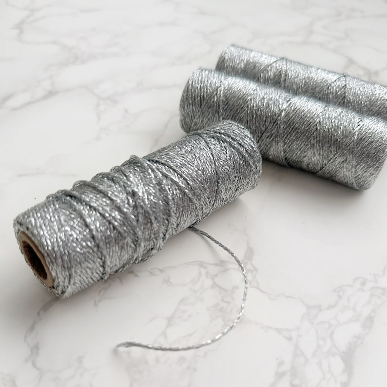 May include: Three spools of silver metallic thread. The thread is wound around cardboard spools.