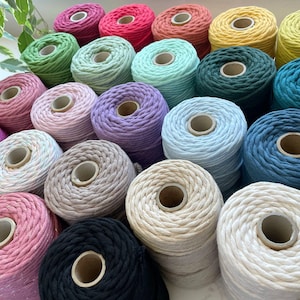 May include: A collection of colourful cotton rope spools in various shades, including pink, green, blue, purple, and beige. The spools are arranged in a semi-circle, showcasing the different colours and textures of the rope.