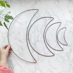 May include: Set of four copper wire crescent moon shapes, arranged in descending size order on a white marble surface.