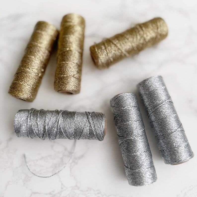 May include: Five spools of metallic thread, two silver and three gold. The thread is wound around cardboard spools.