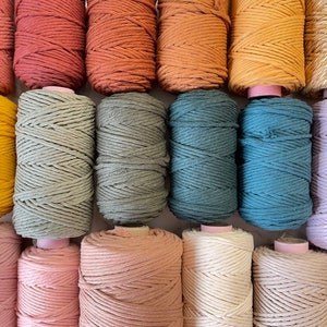 May include: A collection of 15 spools of cotton rope in various colours, including terracotta, mustard yellow, sage green, teal, lavender, and blush pink. The spools are arranged in three rows of five.