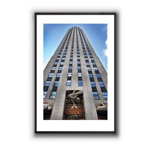 Può includere: Una fotografia in bianco e nero di un grattacielo alto a New York City. L'edificio ha molte finestre e una grande statua in basso. Il testo "All Shall Be Well, The Truth Shall Prevail, The City of the Time" è inciso sulla statua.