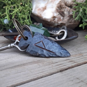 May include: A black metal arrowhead keychain with a silver ring and a small triangle symbol engraved on the front.