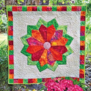 May include: A colorful quilt with a large, red, orange, and green flower design in the center. The quilt is surrounded by a border of red, green, and white squares.