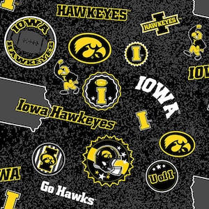 May include: Black fabric with a repeating pattern of Iowa Hawkeyes logos and text. The design includes the team name, the letter "I", a football, and the state outline, all in yellow and white.