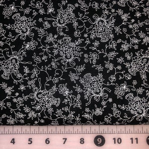 May include: Black fabric with a white floral pattern. The pattern features small flowers, leaves, and baskets of flowers. A ruler is visible at the bottom of the image with numbers 2 through 13.