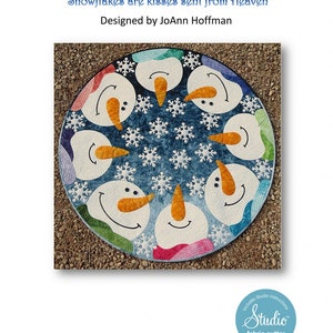 May include: A blue and white fabric quilt with a circle design featuring seven snowmen faces and snowflakes. The quilt is titled "Kisses from Heaven" and includes the text "Snowflakes are kisses sent from Heaven". The quilt is designed by JoAnn Hoffman and includes Studio instructions. The quilt is fabric cutter friendly.
