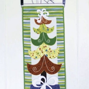 May include: A quilted Christmas tree wall hanging with a green, brown, and blue color scheme. The tree is made of fabric squares and has a white bow on top. The tree is in a blue pot with a white bow.