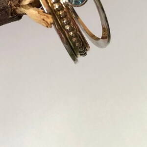 May include: Three gold and silver rings with a blue gemstone. The rings are stacked on top of each other and are on a wooden branch.