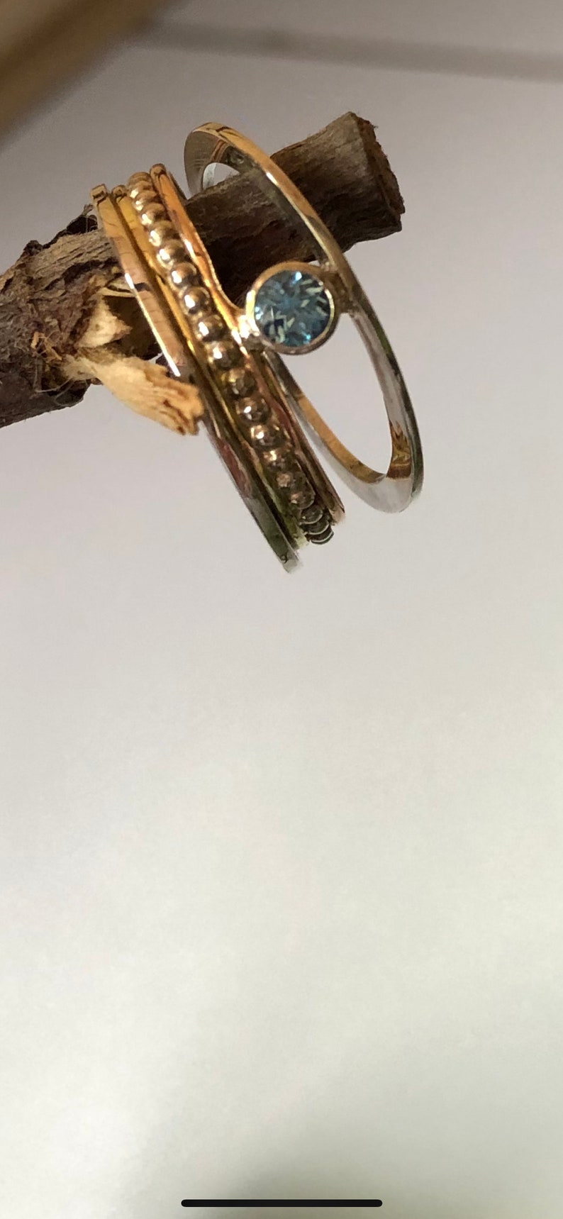 May include: Three gold and silver rings with a blue gemstone. The rings are stacked on top of each other and are on a wooden branch.