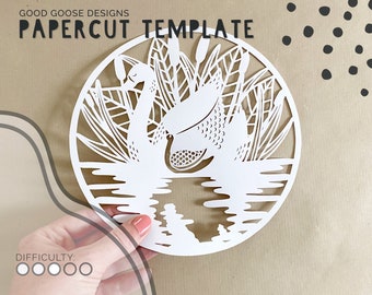 May include: White papercut template of two swans in a pond with reeds. The swans are facing each other and have detailed feathers. The pond is represented by wavy lines and the reeds are represented by long, thin lines. The template is in a circle shape.