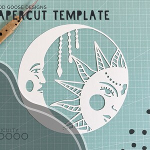 May include: White papercut template of a moon and sun with intricate designs. The moon has a face and the sun has a face with eyelashes. The template is on a blue and white grid background.