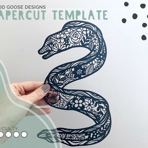 Op de afbeelding: Een zwarte papercut-sjabloon van een paling met ingewikkelde bloemmotieven. Het sjabloon is op een witte achtergrond met zwarte stippen in de rechterbovenhoek. De tekst "GOOD GOOSE DESIGNS PAPERCUT TEMPLATE" staat bovenaan de afbeelding. De tekst "DIFFICULTY" staat linksonder in de afbeelding met vijf cirkels, waarvan er vier zijn ingevuld.
