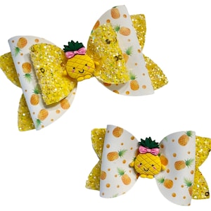 May include: Two yellow and white hair bows with a pineapple design. Each bow has a small, yellow pineapple with a smiling face.