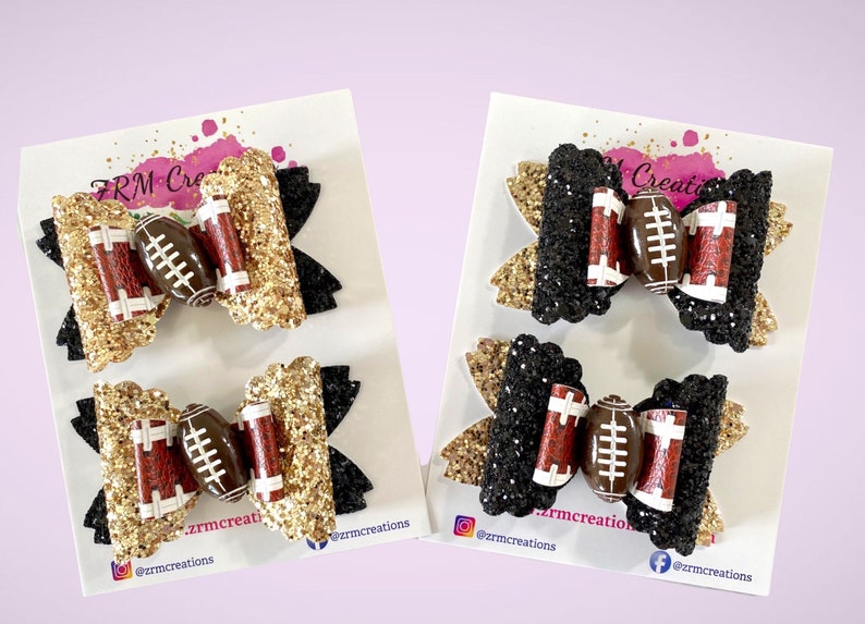 May include: Two pairs of hair bows with a football design. One pair is black and gold glitter, the other is black glitter. Both pairs feature a brown football with white laces.