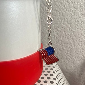 May include: A silver chain necklace with a small American flag charm. The flag is red, white, and blue.