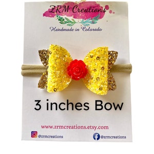K&ouml;nnte beinhalten: Ein 7,6 cm gro&szlig;er gelber Glitzerbogen mit einer roten Blumenmitte auf einem hautfarbenen Haarreif. Der Haarreif wird auf einer wei&szlig;en Karte mit dem Text "ZRM Creations Handmade in Colorado" und der Website-Adresse "www.zrmcreations.etsy.com" gezeigt.