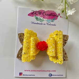 K&ouml;nnte beinhalten: Eine gelbe Glitzer Schleife mit einem roten Rosenakzent. Die Schleife befindet sich auf einer wei&szlig;en Karte mit dem Text "ZRM Creations Handmade in Colorado" und der Website-Adresse "www.zrmcreations.etsy.com".