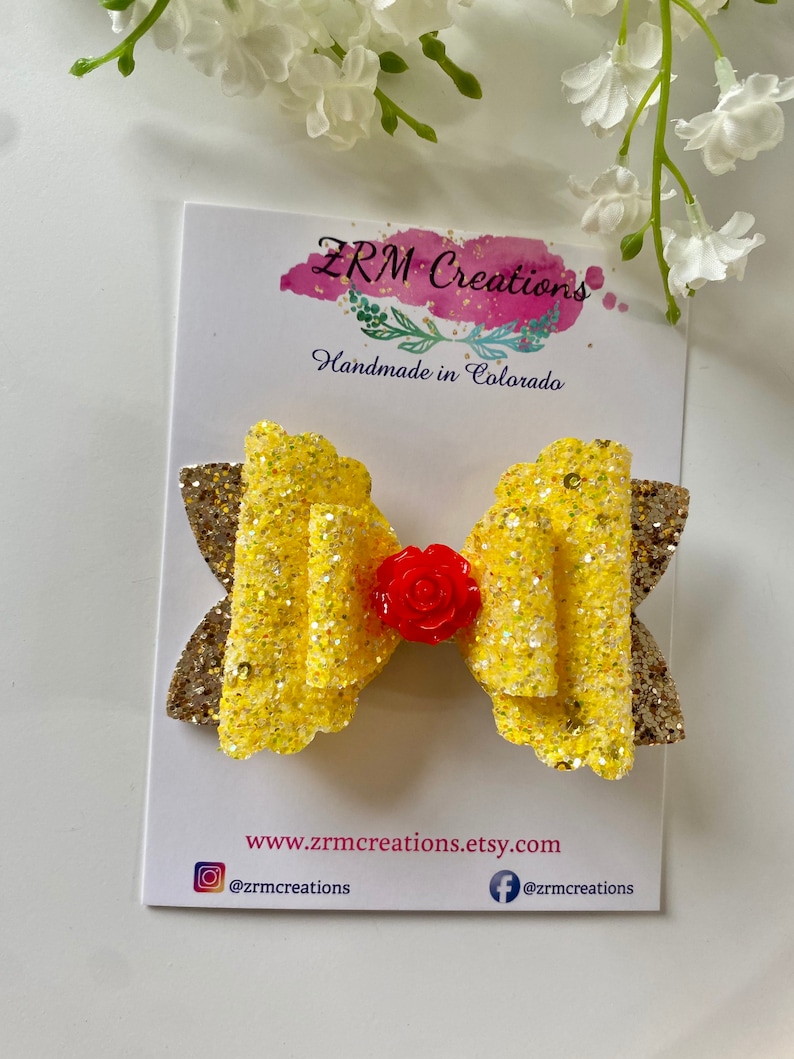 K&ouml;nnte beinhalten: Eine gelbe Glitzer Schleife mit einem roten Rosenakzent. Die Schleife befindet sich auf einer wei&szlig;en Karte mit dem Text "ZRM Creations Handmade in Colorado" und der Website-Adresse "www.zrmcreations.etsy.com".