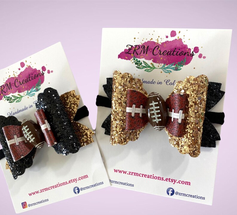 May include: Two hair bows with black and gold glitter and a brown football design. The bows are on white cards with the text "ZRM Creations" and "Handmade in Col" and the website address "www.zrmcreations.etsy.com".