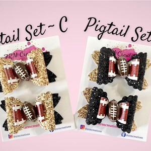 May include: Two sets of pigtail bows with a football design. The first set is gold glitter with black accents and the second set is black glitter with gold accents. Both sets feature a brown and white football.