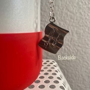 May include: A red and white water bottle with a silver chain and a silver charm that says "Land That I Love".