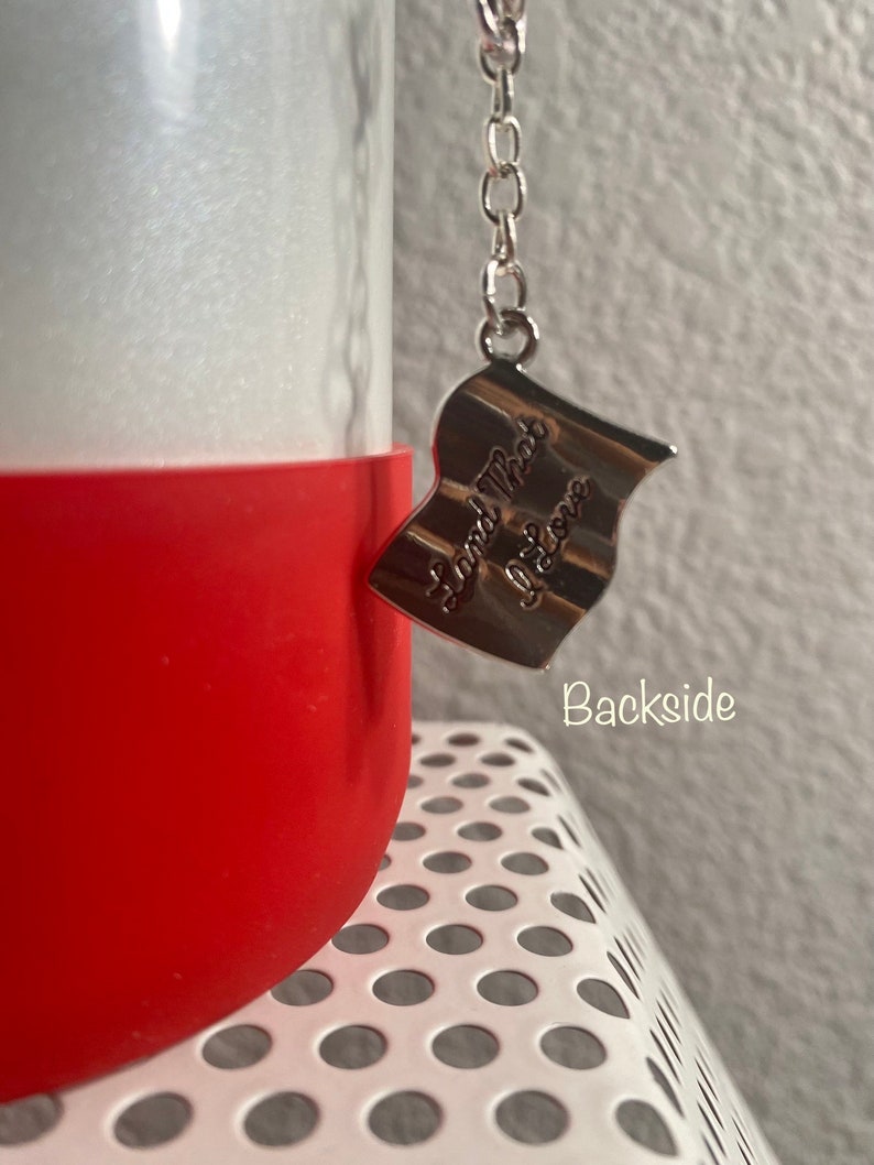 May include: A red and white water bottle with a silver chain and a silver charm that says "Land That I Love".