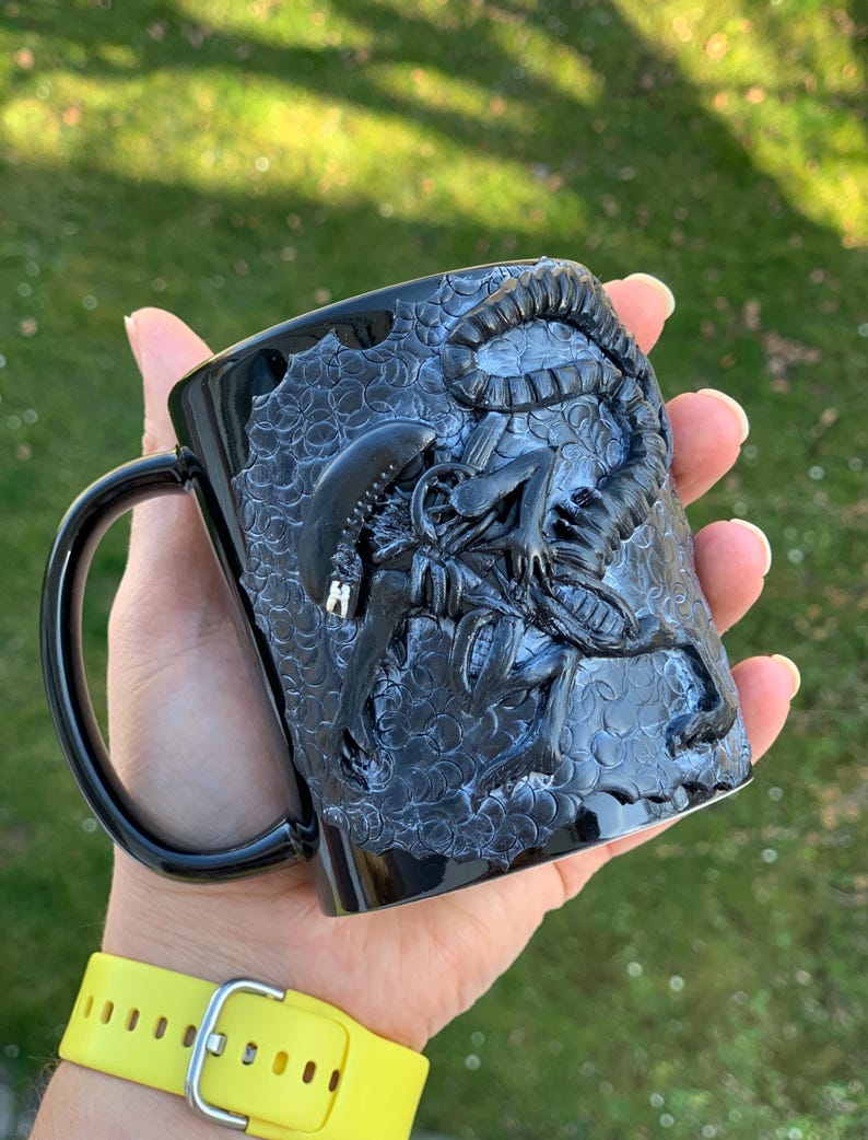 Peut inclure: Mug en c&eacute;ramique noire avec un motif d'extraterrestre sculpt&eacute; en 3D. La tasse a une surface textur&eacute;e et une poign&eacute;e noire.