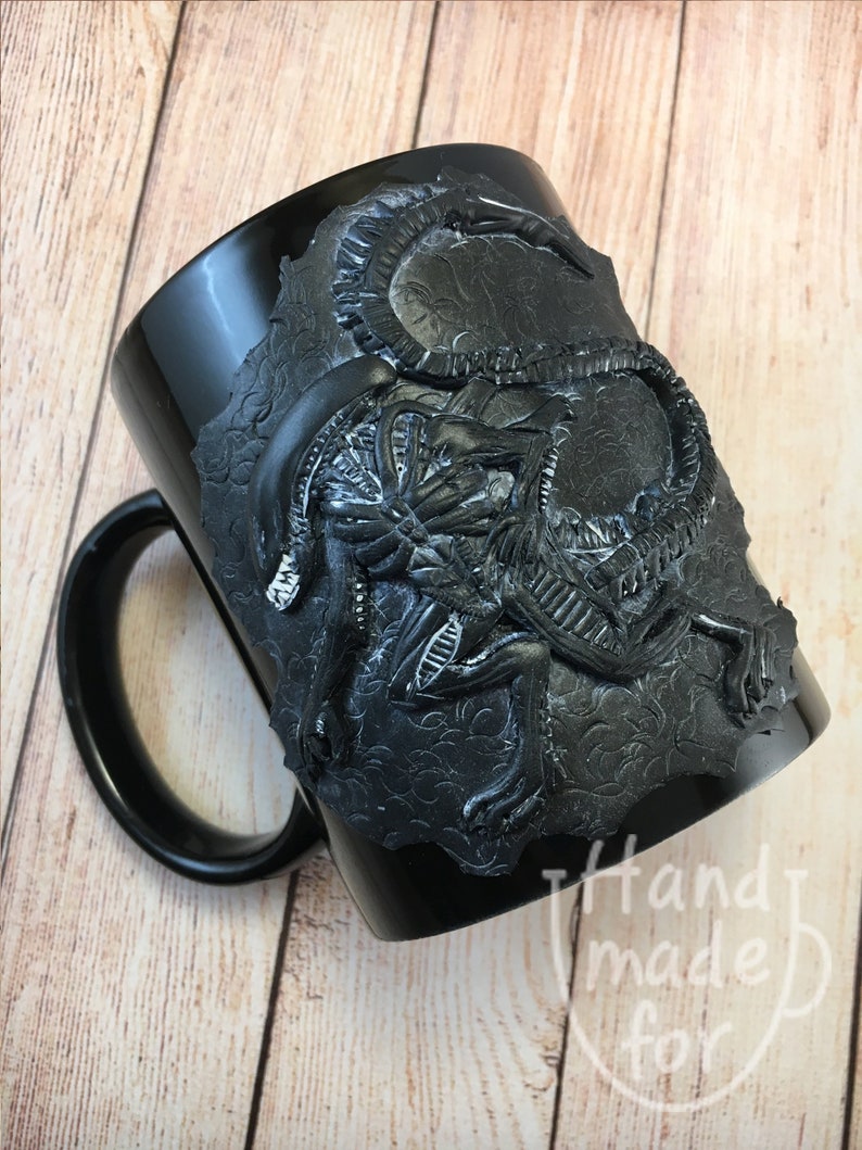 Peut inclure: Mug en c&eacute;ramique noire avec un motif sculpt&eacute; en 3D d'une cr&eacute;ature extraterrestre. La tasse a une poign&eacute;e noire et l'extraterrestre est sculpt&eacute; dans un style noir textur&eacute;.