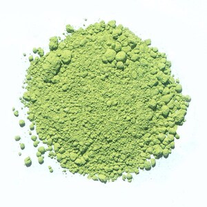 May include: A close-up of a pile of bright green matcha powder on a white surface.