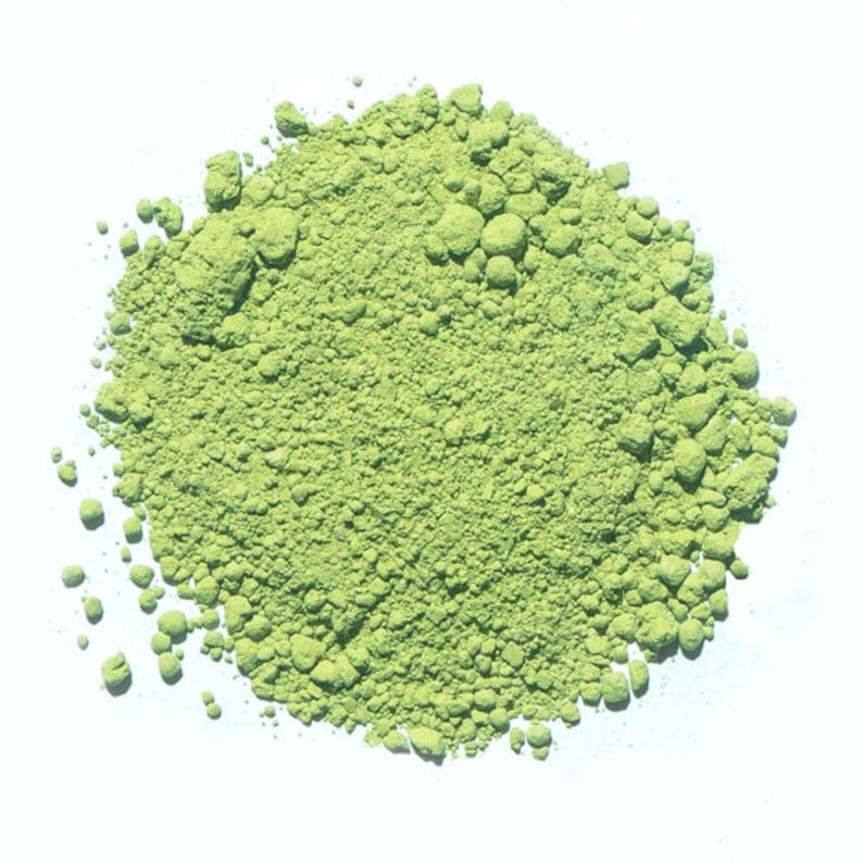 May include: A close-up of a pile of bright green matcha powder on a white surface.