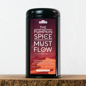 May include: A black metal tea tin with a red, orange, and white label. The label reads "The Pumpkin Spice Must Flow - Limited Edition". The ingredients are listed as "Pu'erh tea, cinnamon, clove, ginger root, cardamom, N&A flavor". The brewing instructions are "5 min | 4g | 175°F | High Caffeine". The website address "novelteatins.com" is printed at the bottom of the label.