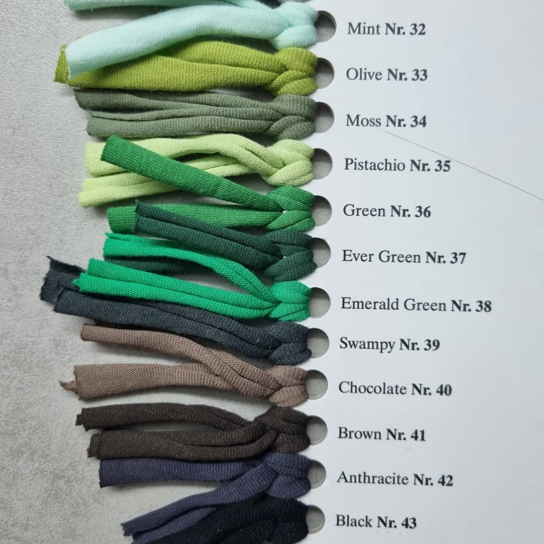 May include: A color chart of fabric swatches in various shades of green, brown, and black. The swatches are labeled with their corresponding color names and numbers, starting with Mint Nr. 32 and ending with Black Nr. 43.