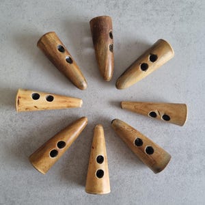 May include: Eight brown wooden toggles with two holes each, arranged in a circle on a gray surface.