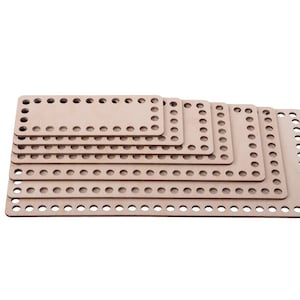 Może przedstawiać: Zestaw sześciu drewnianych krosna tkackich w różnych rozmiarach, ułożonych jeden na drugim. Krosna są jasnobrązowe i mają szereg równomiernie rozmieszczonych otworów wokół krawędzi.