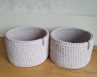 Può includere: Due cesti di stoccaggio in crochet rosa chiaro con una trama tessuta. I cesti sono rotondi e hanno un leggero bordo attorno alla parte superiore.